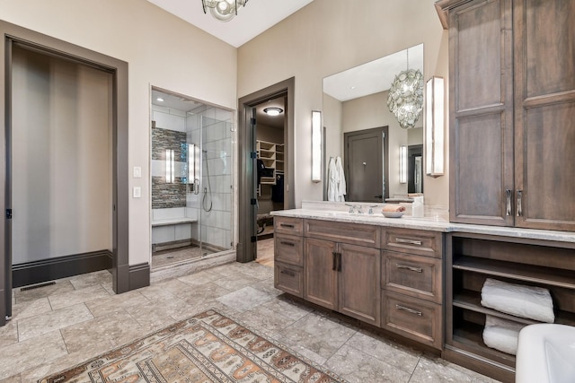 bathroom featuring a chandelier, vanity, baseboards, stone finish flooring, and a walk in closet