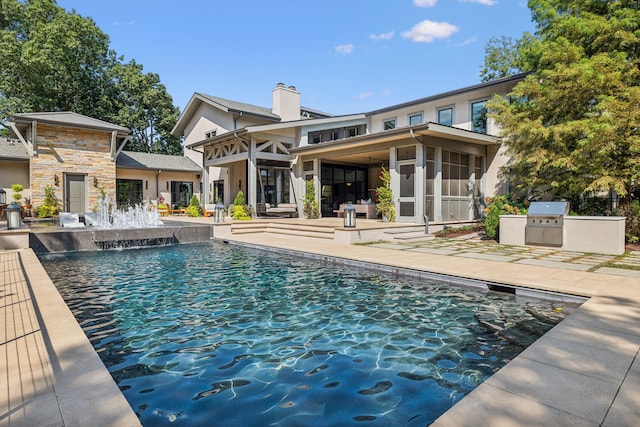 outdoor pool featuring a sunroom, a grill, a patio area, and an outdoor kitchen