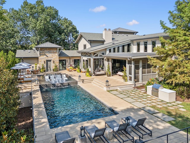 pool featuring an in ground hot tub, exterior kitchen, a patio area, and a sunroom