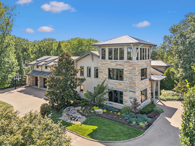 view of front of property with driveway, stone siding, metal roof, a standing seam roof, and stucco siding