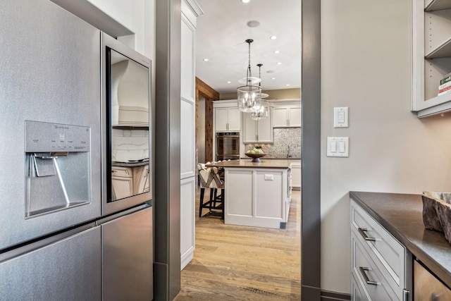 kitchen with a breakfast bar area, stainless steel appliances, light wood finished floors, dark countertops, and tasteful backsplash