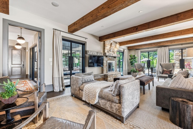 living area with baseboards, beamed ceiling, and a stone fireplace