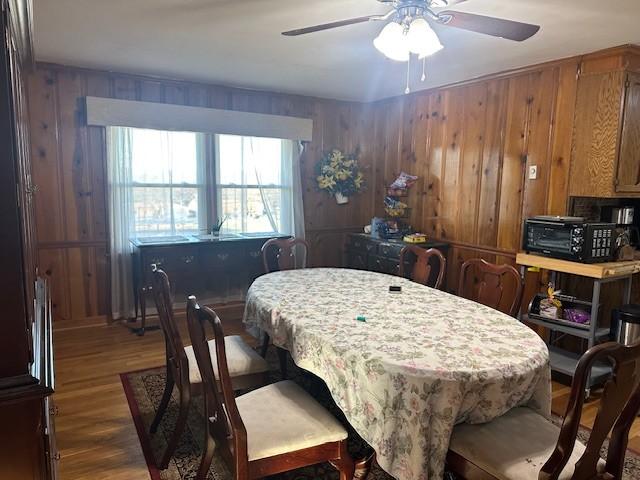 dining area with wood walls, dark wood-style flooring, and a ceiling fan