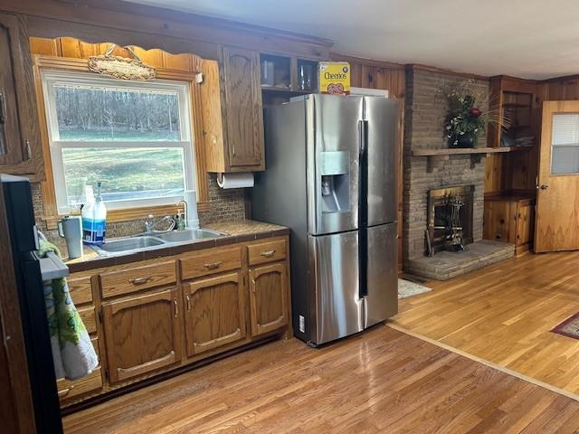 kitchen with tile counters, tasteful backsplash, light wood-style flooring, a sink, and stainless steel fridge