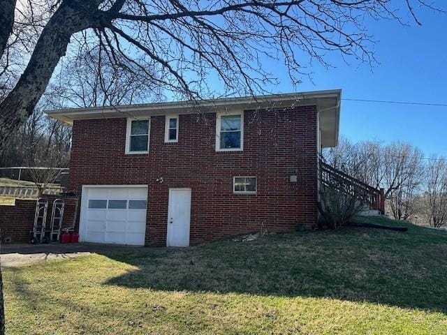 view of side of home with a yard, brick siding, an attached garage, and driveway