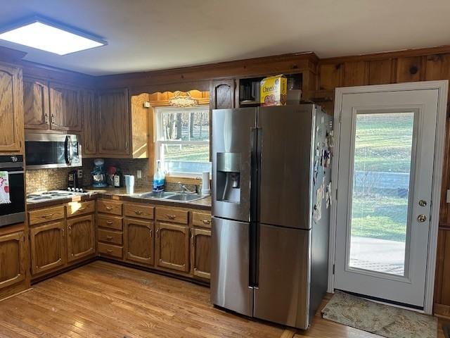 kitchen featuring brown cabinets, stainless steel appliances, a wealth of natural light, a sink, and light wood-type flooring