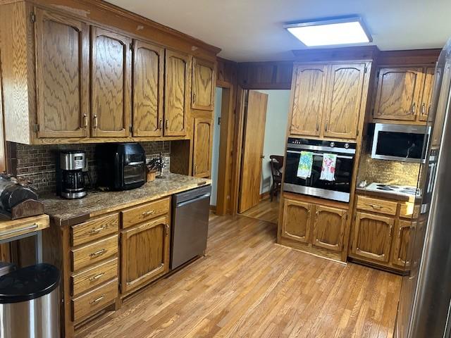 kitchen with appliances with stainless steel finishes, brown cabinetry, light wood finished floors, and tasteful backsplash