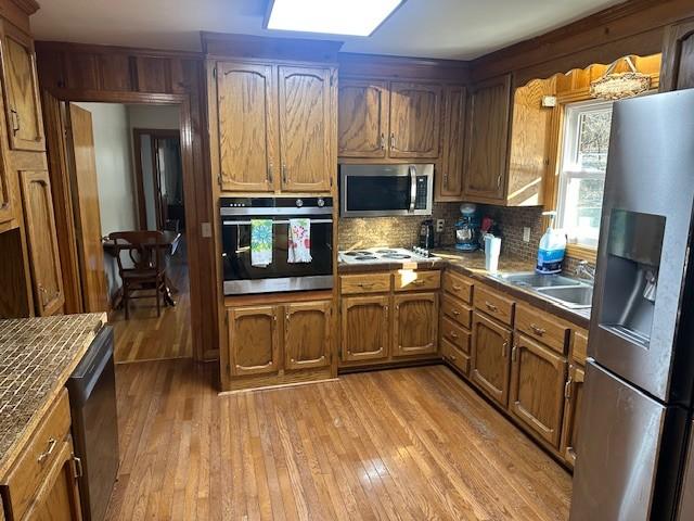 kitchen with stainless steel appliances, dark countertops, brown cabinets, and light wood-style flooring