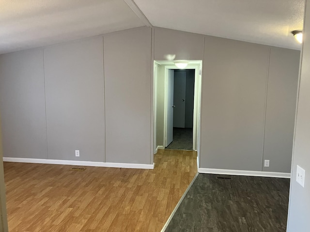 spare room featuring light wood-type flooring, visible vents, and lofted ceiling