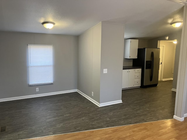 kitchen featuring baseboards, white cabinets, stainless steel refrigerator with ice dispenser, dark wood-style floors, and dark countertops