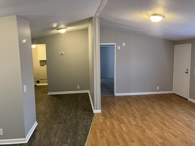 unfurnished room featuring a textured ceiling, wood finished floors, lofted ceiling, and baseboards