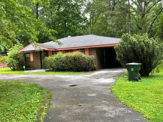 ranch-style home with aphalt driveway, a carport, brick siding, and a front lawn