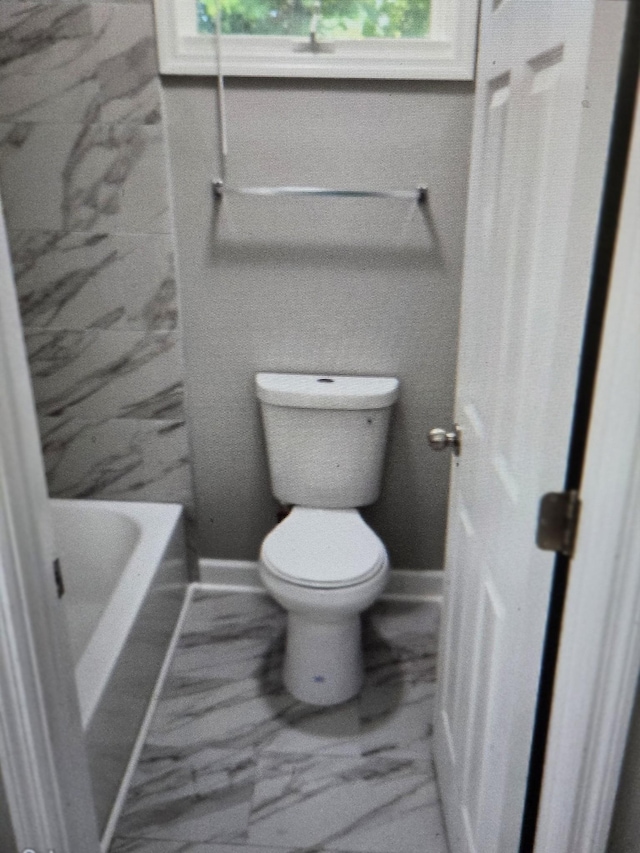 full bathroom with a tub, marble finish floor, baseboards, and toilet