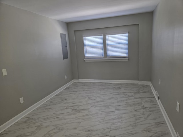 empty room featuring marble finish floor, electric panel, and baseboards