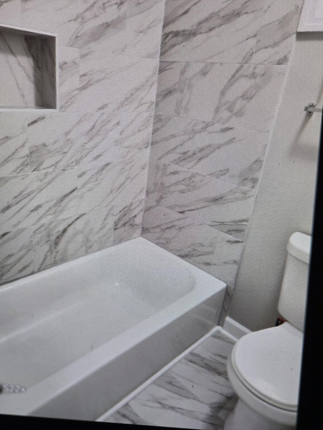 bathroom with toilet, marble finish floor, and a bath