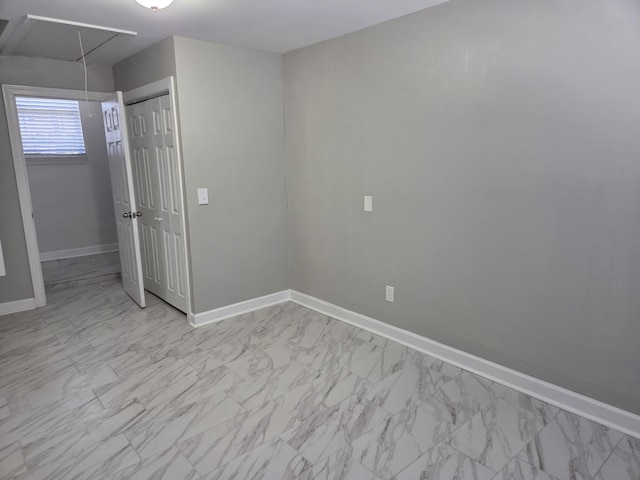 unfurnished bedroom featuring marble finish floor, a closet, attic access, and baseboards