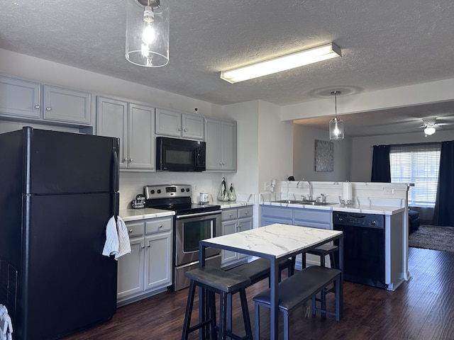 kitchen featuring a peninsula, dark wood-type flooring, a sink, light countertops, and black appliances