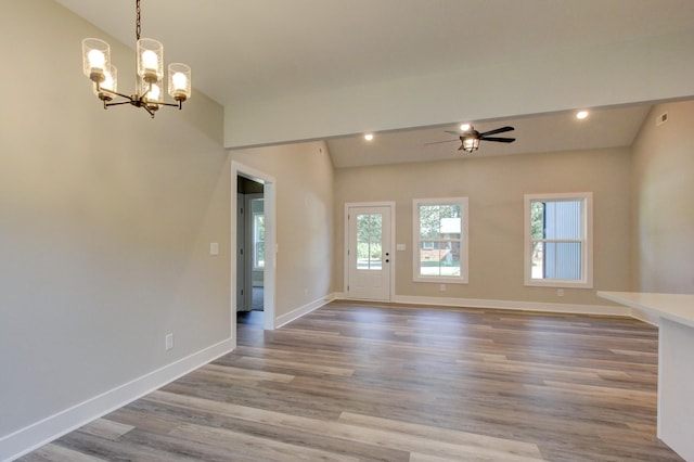 empty room with recessed lighting, ceiling fan with notable chandelier, wood finished floors, baseboards, and vaulted ceiling