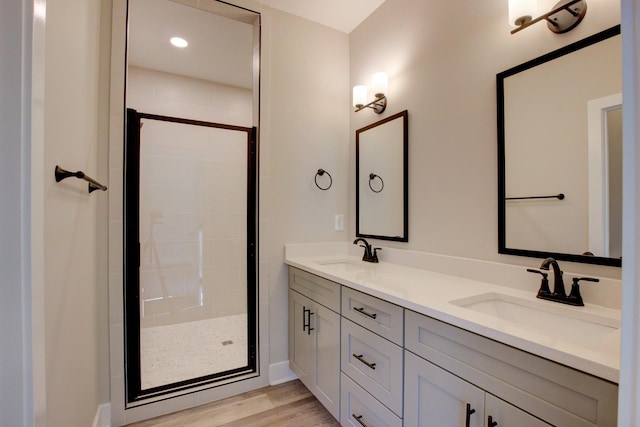 bathroom featuring double vanity, wood finished floors, a stall shower, and a sink