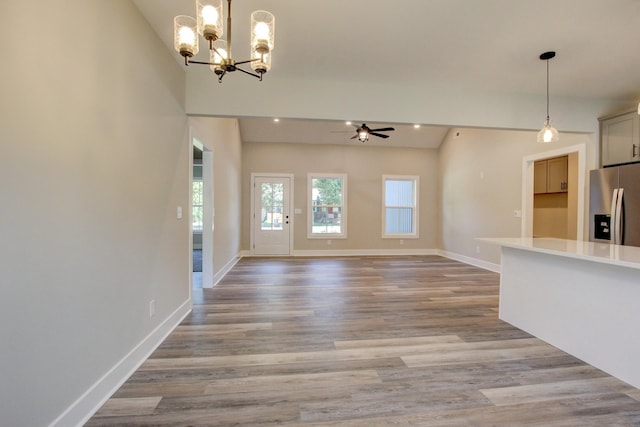 unfurnished living room with ceiling fan with notable chandelier, light wood-type flooring, and baseboards