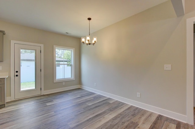 spare room with an inviting chandelier, baseboards, and wood finished floors