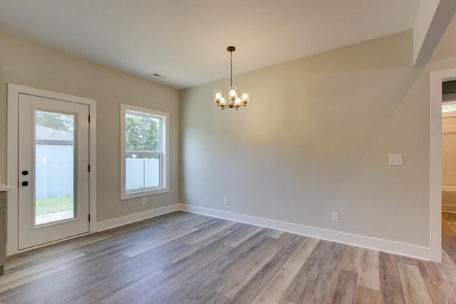 unfurnished room featuring visible vents, light wood-type flooring, an inviting chandelier, and baseboards