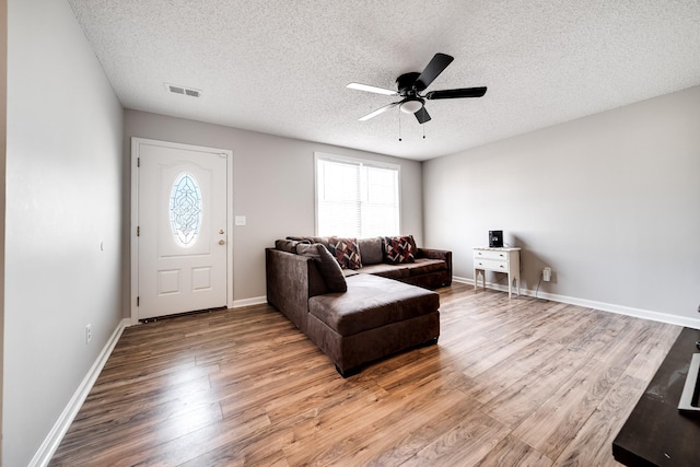 living area featuring baseboards, visible vents, a ceiling fan, wood finished floors, and a textured ceiling