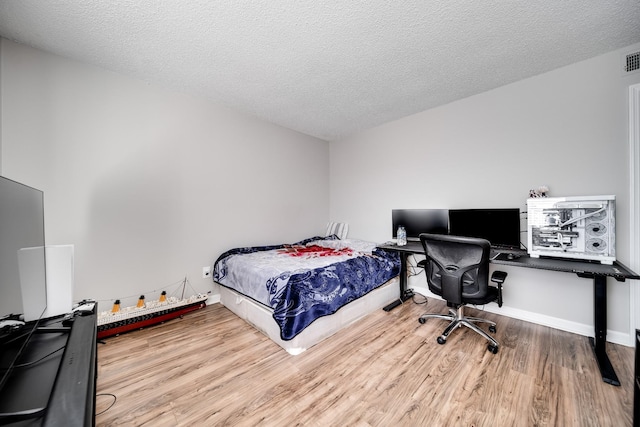 bedroom with visible vents, a textured ceiling, baseboards, and wood finished floors