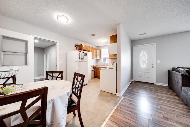 dining space featuring visible vents, light wood-style flooring, baseboards, and a textured ceiling