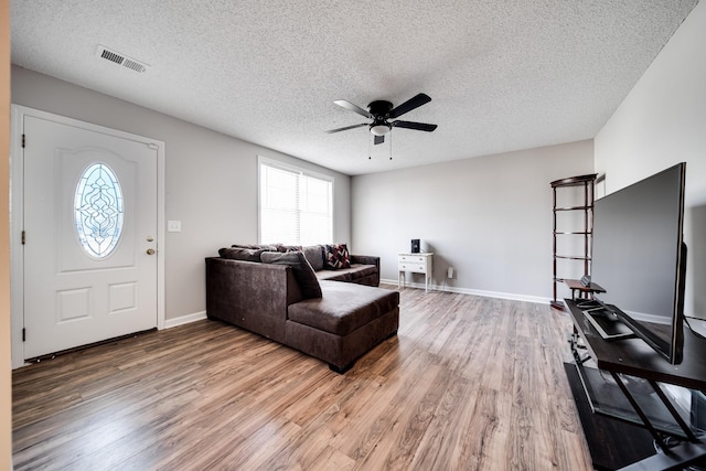 living room featuring visible vents, a textured ceiling, baseboards, and wood finished floors