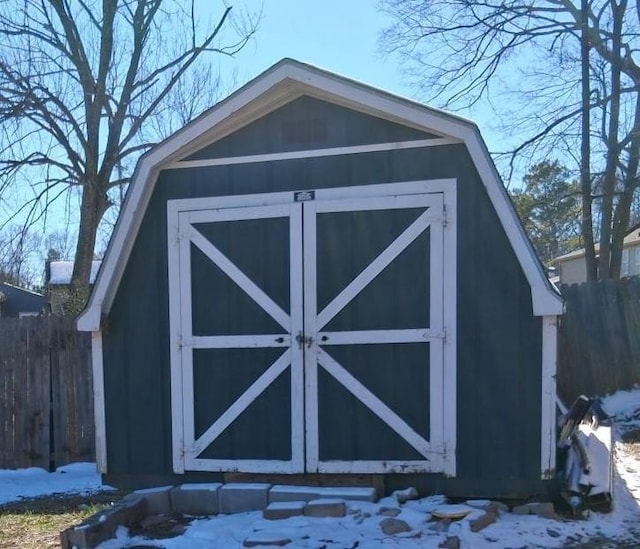 snow covered structure featuring fence, an outdoor structure, and a storage unit