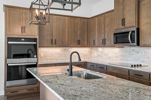 kitchen featuring appliances with stainless steel finishes, decorative light fixtures, a sink, light stone countertops, and backsplash