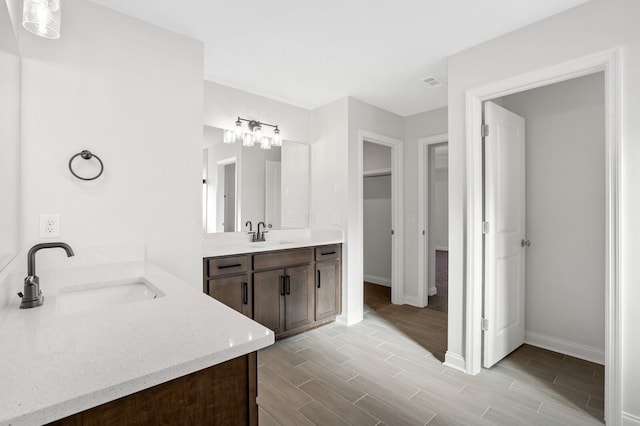 full bath featuring two vanities, visible vents, wood tiled floor, a sink, and baseboards