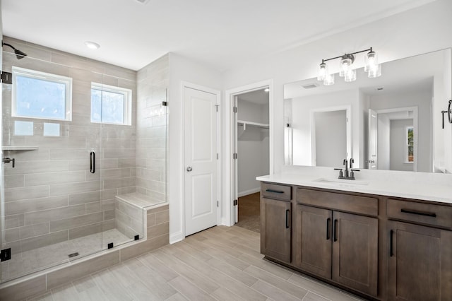 bathroom with a stall shower, baseboards, wood finished floors, a walk in closet, and vanity