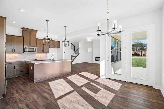 kitchen with a center island with sink, light countertops, stainless steel microwave, decorative backsplash, and a chandelier