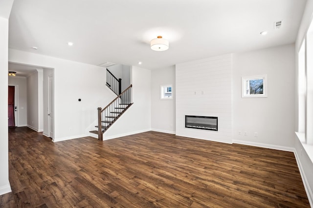 unfurnished living room featuring a large fireplace, dark wood-type flooring, visible vents, baseboards, and stairway