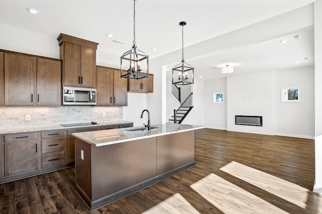 kitchen with stainless steel microwave, a sink, black electric cooktop, a fireplace, and backsplash