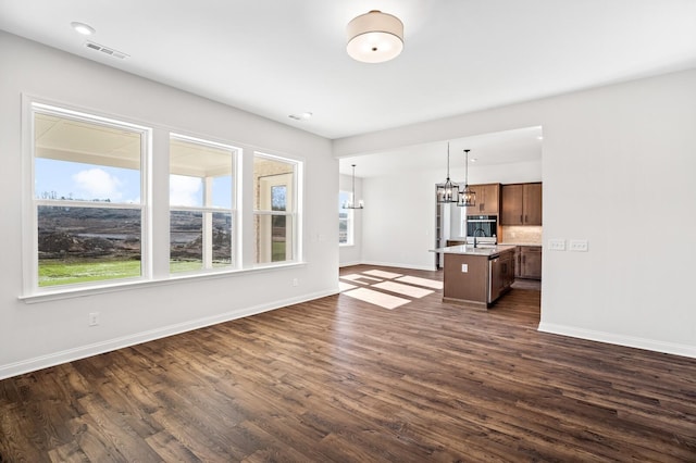 unfurnished living room with visible vents, dark wood-type flooring, a sink, a chandelier, and baseboards