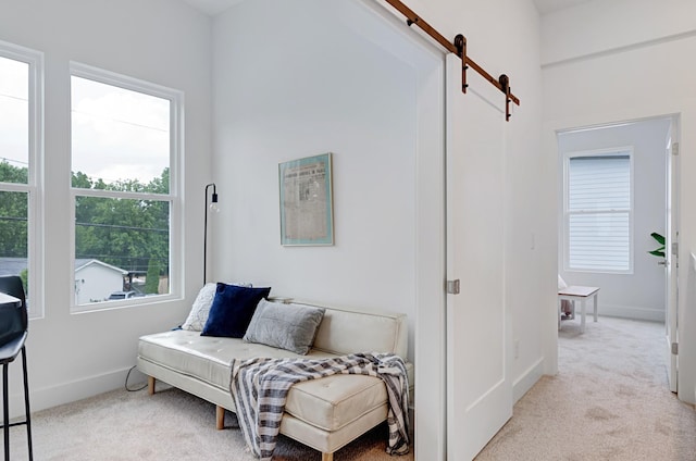 sitting room with light carpet, a barn door, and baseboards