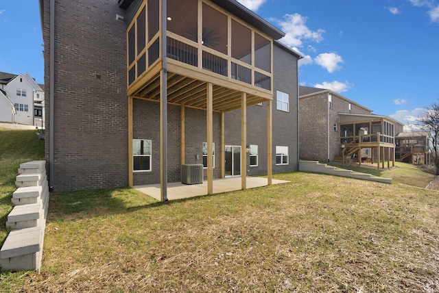 rear view of property with a patio, central air condition unit, brick siding, a sunroom, and a lawn