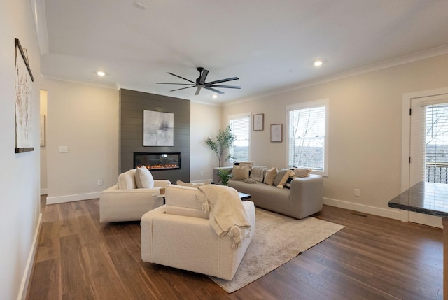 living area with a large fireplace, baseboards, ornamental molding, and dark wood finished floors