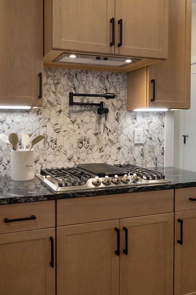 kitchen with tasteful backsplash, extractor fan, dark stone countertops, and stainless steel gas stovetop