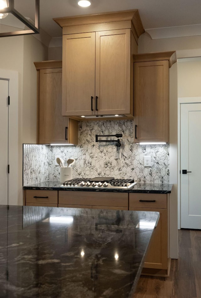 kitchen with dark stone counters, stainless steel gas stovetop, backsplash, and wood finished floors