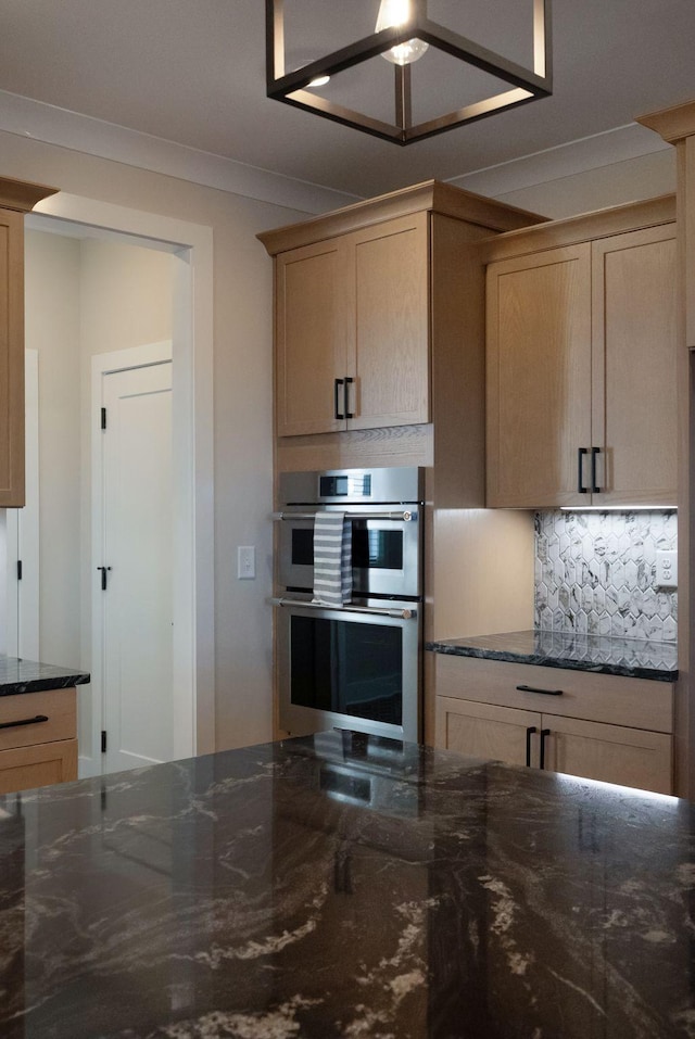 kitchen with dark stone counters, crown molding, stainless steel double oven, and decorative backsplash