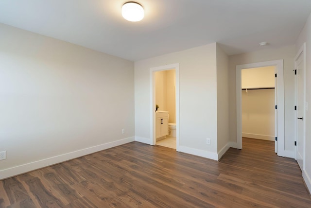 unfurnished bedroom featuring dark wood finished floors, a closet, a spacious closet, ensuite bath, and baseboards