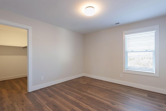 unfurnished bedroom with a walk in closet, a closet, visible vents, dark wood-type flooring, and baseboards