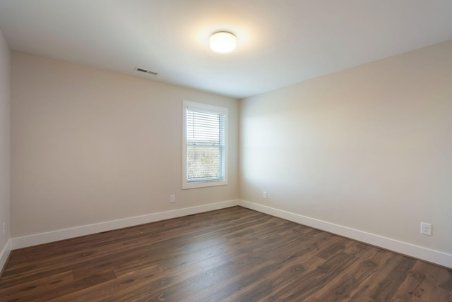 spare room featuring visible vents, baseboards, and dark wood-style flooring