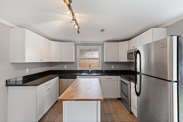 kitchen with stainless steel appliances, a sink, visible vents, white cabinetry, and a center island