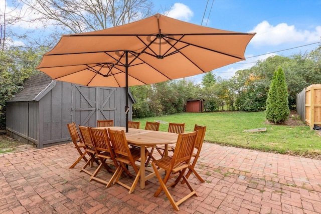 view of patio / terrace featuring fence, a storage unit, an outbuilding, and outdoor dining space