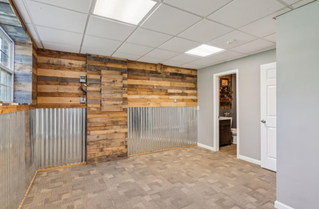 spare room with wooden walls, carpet, baseboards, and a drop ceiling
